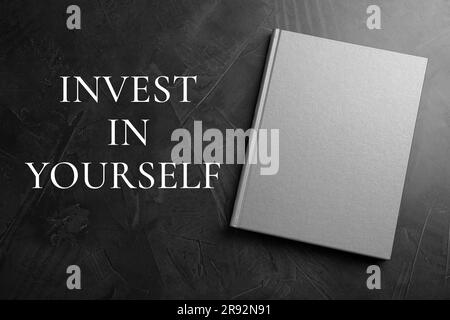 Investite in voi stessi, affermazione. Libro e parole sul tavolo nero, vista dall'alto Foto Stock