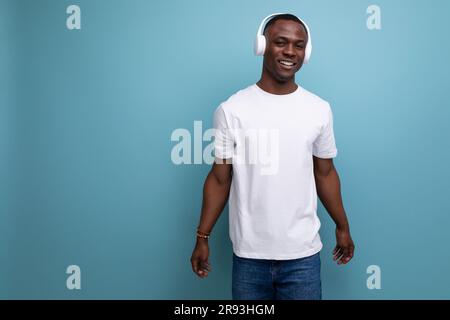 giovane africano con t-shirt bianca che ascolta musica con cuffie bianche sullo sfondo dello studio con spazio per la copia Foto Stock