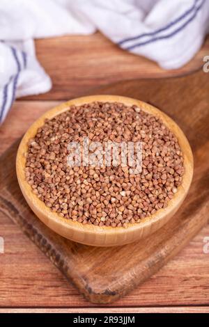 Grano saraceno su fondo di legno. Grani di grano saraceno in un recipiente di legno Foto Stock