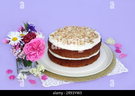 Torta di carote e noci con fiori estivi su sfondo viola. Piatti deliziosi fatti in casa per tè pomeridiano o feste di compleanno. Foto Stock