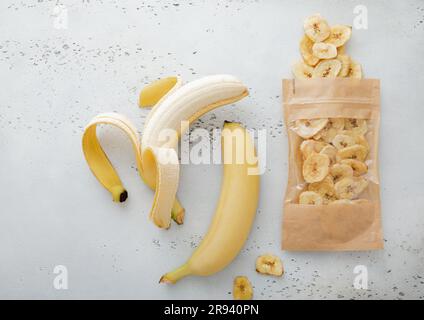 Banane fresche crude sane con pacchetto di patatine di banana secche su tavola leggera. Vista dall'alto. Foto Stock