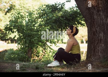 Bella ragazza sorridente mentre si siede vicino all'albero nel parco Foto Stock