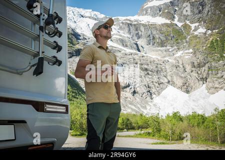 Un turista caucasico di 40 anni che si gusta un caffè mattutino accanto allo Scenic Glacier e soggiorna accanto al camper Van nella contea di Vestland in Norvegia. Foto Stock