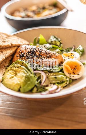 Insalata di foglie fresche servita con avocado, uova e salmone alla griglia in cima costellato di sesamo. Foto Stock