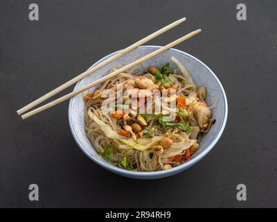 Gamberetti freschi, spaghetti saporiti, verdure nutrienti e arachidi croccanti serviti in un'elegante ciotola bianca con bastoncini. Foto Stock
