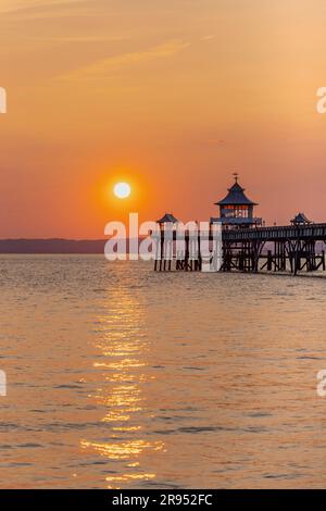 Clevedon Pier al tramonto con un sole luminoso e una striscia di luce solare che attraversa il mare Foto Stock