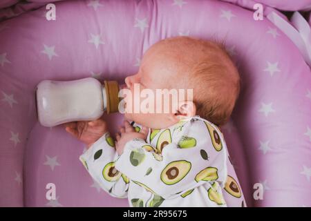 Un neonato beve autonomamente latte o una miscela secca da un biberon, a casa Foto Stock