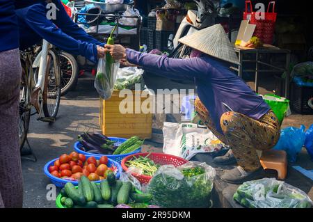 Acquisto e vendita: Una transazione avviene in una bancarella di verdure improvvisata nel mercato di Hoi An nella città vecchia di Hoi An, in Vietnam. Foto Stock