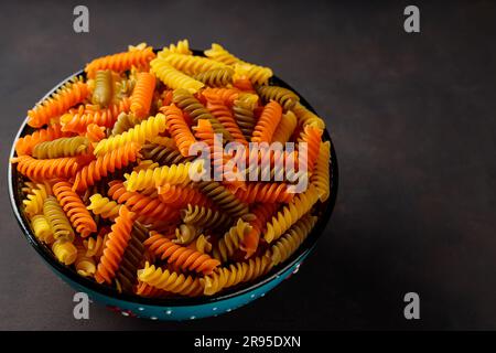 Fusilli pasta secca su fondo scuro. Fusilli tricolore in una ciotola. Vista dall'alto. Spazio di copia Foto Stock