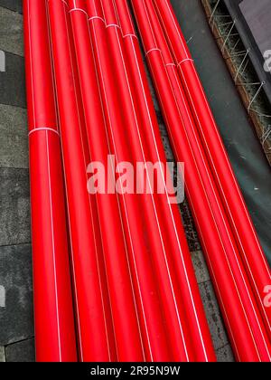 Tubi in plastica rossa per comunicazioni impilati sul marciapiede Foto Stock