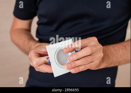 Un elettricista tiene in mano una lampadina a LED di una lampada da soffitto. Primo piano. Foto Stock