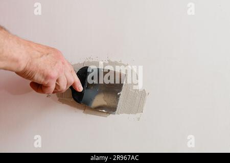 Riparazione dei fori nel muro a secco. Un tuttofare sta riparando un buco nel muro a secco del muro. Foto Stock