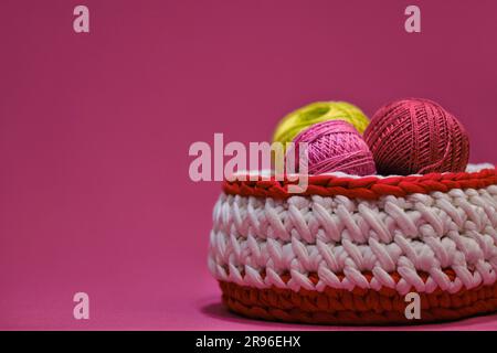 Concept hobby artigianale per ricci da casa. Filati per uncinetto. Diverse palline di lana multicolore di filo in un cestino di vimini su un dorso rosa Foto Stock
