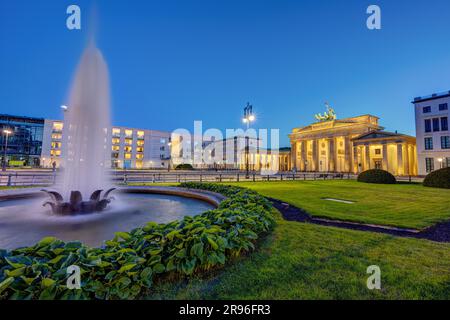 La porta di Brandeburgo illuminata a Berlino al tramonto con una fontana Foto Stock