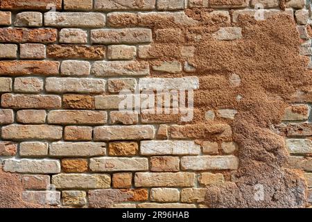 Sfondo di un muro di mattoni rosso rotto con resti di intonaco Foto Stock