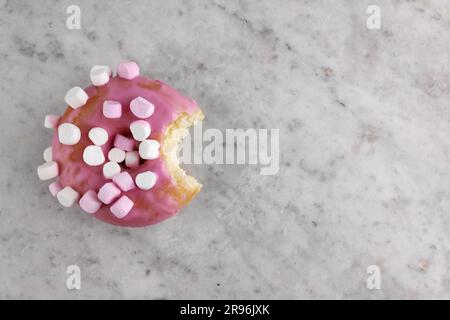 Ciambella con glassa rosa e marshmallow piccoli con un boccone mancante. Foto Stock