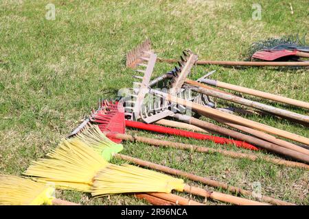 Rastrelli, pale, spazzatrici e spazzole, inventario domestico per la pulizia, disposizione del territorio, scavo della terra giacciono sull'erba verde Foto Stock