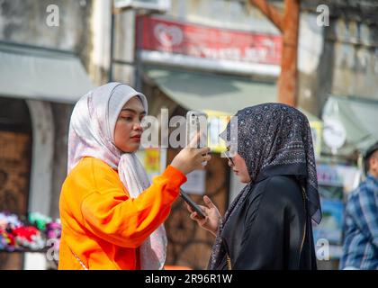 24 febbraio 2023- George Town -Penang-Malesia-due giovani donne vestite di arancione e nero con una sciarpa tradizionale sulla testa scattano foto Foto Stock