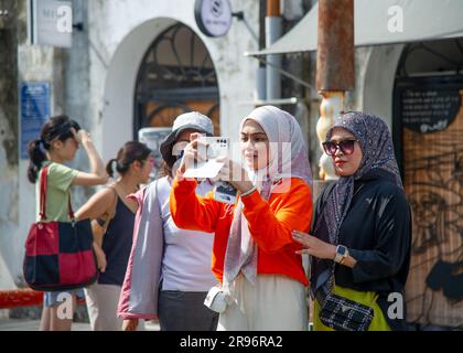 24 febbraio 2023- George Town -Penang-Malesia-due giovani donne vestite di arancione e nero con una sciarpa tradizionale sulla testa scattano foto Foto Stock