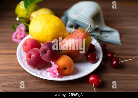 Albicocche fresche limoni pere e ciliegie dolci sul piatto bianco Foto Stock