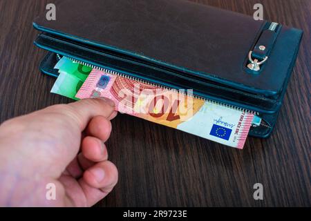 La mano dell'uomo tira fuori i conti con una borsa di pelle e il ritiro della moneta europea euro, euro Foto Stock