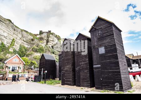Storici negozi di reti asfaltate per il deposito di reti da pesca allo Stade, al castello di Hastings sullo sfondo, ad Hastings, in Inghilterra Foto Stock