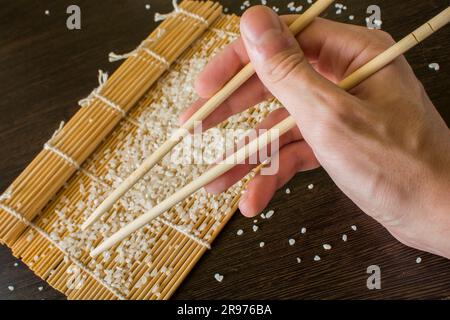 bacchette in mano sullo sfondo di un sushi mat Foto Stock