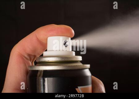 Vista ravvicinata di una mano umana e di una bottiglia di spray compressa isolata su uno sfondo nero Foto Stock