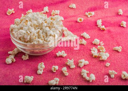 popcorn in un piatto di vetro, su uno sfondo rosa irregolare Foto Stock