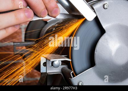 Un affilatore e una mano con una lama su un tavolo di legno, da vicino sullo sfondo di una parete di mattoni Foto Stock