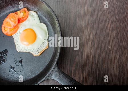 uova fritte con pomodori tritati in una padella in ghisa su un tavolo di legno Foto Stock