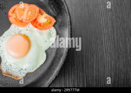 uova fritte con pomodori tritati in una padella in ghisa su un tavolo di legno Foto Stock