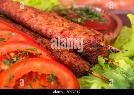 kebab lulia fritto adagiato su un'insalata con pomodori e aneto con prezzemolo adagiato su un albero sullo sfondo di una parete di mattoni Foto Stock