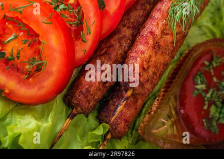 kebab lulia fritto adagiato su un'insalata con pomodori e aneto con prezzemolo adagiato su un albero sullo sfondo di una parete di mattoni Foto Stock