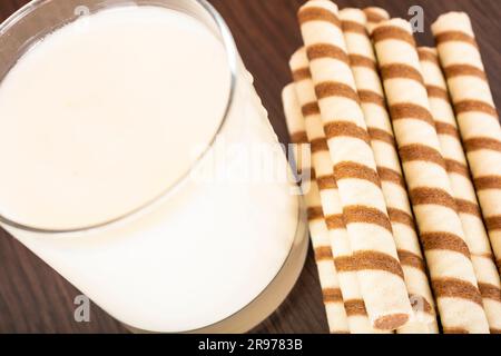 un bicchiere di yogurt con un tubulo a cialda su sfondo nero e una parete in mattoni, spazio libero per il testo, luce naturale Foto Stock