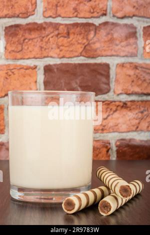 un bicchiere di yogurt con un tubulo a cialda su sfondo nero e una parete in mattoni, spazio libero per il testo, luce naturale Foto Stock