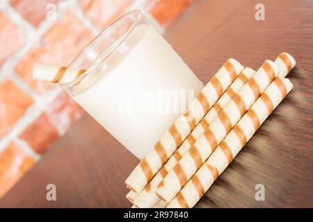 un bicchiere di yogurt con un tubulo a cialda su sfondo nero e una parete in mattoni, spazio libero per il testo, luce naturale Foto Stock