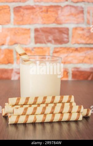 un bicchiere di yogurt con un tubulo a cialda su sfondo nero e una parete in mattoni, spazio libero per il testo, luce naturale Foto Stock