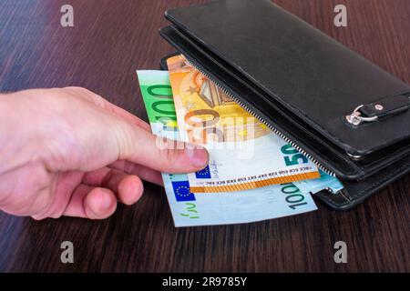 La mano dell'uomo tira fuori i conti con una borsa di pelle e il ritiro della moneta europea euro, euro Foto Stock