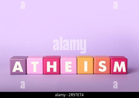 Ateismo delle parole fatto di cubi con lettere su sfondo viola Foto Stock