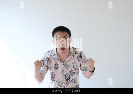 Un giovane asiatico che indossa una camicia rosa con motivi tropicali e uno smartwatch sul polso sinistro si sente felice ed eccitato e mostra la sua espressione Foto Stock