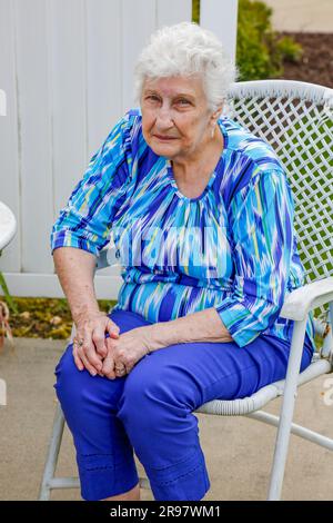 Una donna anziana di colore blu si siede su una sedia bianca sul patio dietro la sua casa a Warren, Indiana, Stati Uniti. Foto Stock