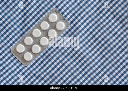 Confezione di compresse rotonde di farmaci farmaceutici su un panno di tessuto a scacchi bianco-blu. Vista dall'alto degli integratori alimentari in blister. Foto Stock