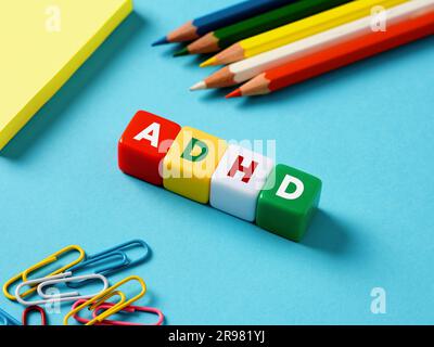 Disturbo da deficit di attenzione iperattività concetto ADHD. L'abbreviazione ADHD su cubi colorati con oggetti di cancelleria su sfondo blu. Foto Stock