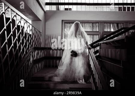 Ghost of Bride in Haunted House, misteriosa donna in abito bianco in piedi sulle scale dell'edificio abbandonato, sfondo dell'orrore per halloween Foto Stock