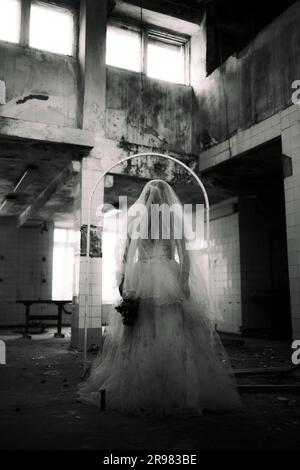 Scena horror di Halloween, sposa fantasma con un abito bianco in un edificio in rovina, foto in bianco e nero Foto Stock