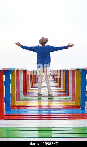 Man Opening Arms sul Molo in legno multicolore Foto Stock