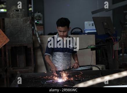 Giacarta, Indonesia - 20 giugno 2023: Un operaio taglia lastre di ferro con una tosatrice Foto Stock