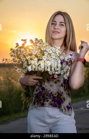 Bella ragazza con margherite sullo sfondo del tramonto. Foto Stock