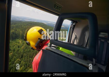 Soccorso su terreni difficili da raggiungere. Paramedico di Helicopter Emergency Medical Service guardando in basso dalla porta aperta dell'elicottero. Foto Stock